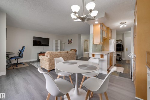 Open concept living area featuring light gray walls, gray flooring, a kitchen with light wood cabinetry, and a dining area with a modern light fixture - 1202 9909 110 Street Nw, Edmonton, AB - Indoor Photo Showing Dining Room