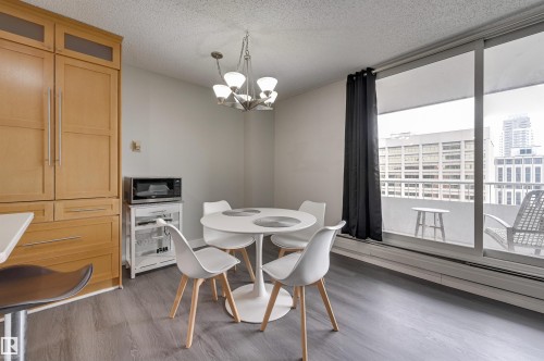 Living area featuring light grey flooring, a dining area with a contemporary chandelier, and a balcony with city views - 1202 9909 110 Street Nw, Edmonton, AB - Indoor Photo Showing Dining Room