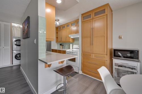 The property features a kitchen with light wood cabinetry, light countertops, and a subway tile backsplash - 1202 9909 110 Street Nw, Edmonton, AB - Indoor With Fireplace