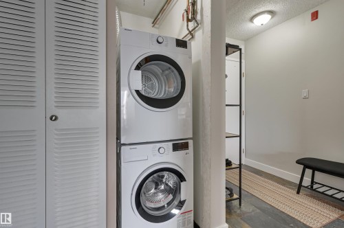 This property features a dedicated laundry area with a stacked washer and dryer, louvered bi-fold doors, and slate flooring - 1202 9909 110 Street Nw, Edmonton, AB - Indoor Photo Showing Laundry Room