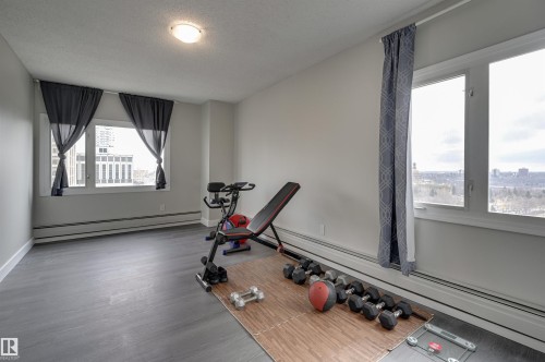 Spacious room featuring light gray walls, dark gray flooring, and multiple windows providing natural light - 1202 9909 110 Street Nw, Edmonton, AB - Indoor Photo Showing Gym Room