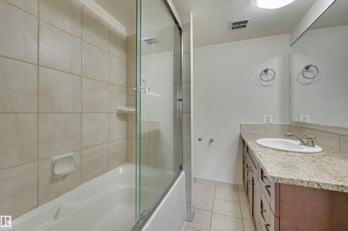 Bathroom featuring a tub with a glass shower enclosure, beige tiled walls, a vanity with a granite countertop, and a large mirror - 1202 9909 110 Street Nw, Edmonton, AB - Indoor Photo Showing Bathroom