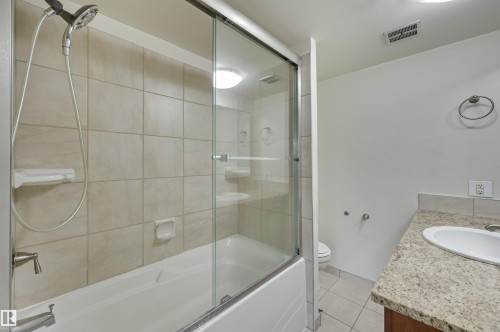 Bathroom featuring a combination bathtub and shower with sliding glass doors and tiled walls - 1202 9909 110 Street Nw, Edmonton, AB - Indoor Photo Showing Bathroom