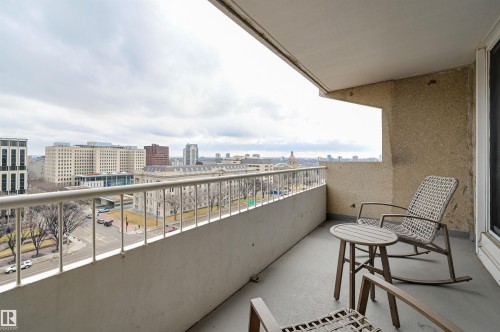 This property features an outdoor balcony with a light-colored railing, offering expansive views of surrounding buildings and a street below - 1202 9909 110 Street Nw, Edmonton, AB - Outdoor With Balcony With Exterior