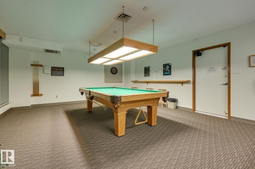 The recreational space features a pool table with an overhead light fixture, a dartboard, and carpeted flooring - 1202 9909 110 Street Nw, Edmonton, AB - Indoor Photo Showing Other Room