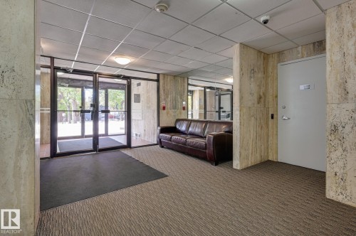 The property features a welcoming lobby area with glass entry doors, carpeted flooring, and stone-clad walls - 1202 9909 110 Street Nw, Edmonton, AB - Indoor Photo Showing Other Room