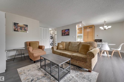 The property features a bright living area with hard surface flooring throughout, a compact dining space, and a kitchen with wooden cabinetry - 1202 9909 110 Street Nw, Edmonton, AB - Indoor Photo Showing Living Room
