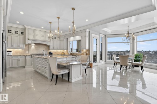 Spacious kitchen and dining area featuring light-toned cabinetry, granite countertops, an island with seating, polished tile flooring, and large windows offering expansive views - 1413 Woodward Crescent, Edmonton, AB - Indoor