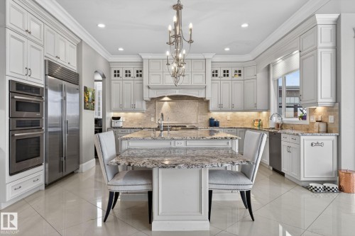 Well-appointed kitchen featuring a large central island with a granite countertop, a stainless steel refrigerator, and integrated double ovens - 1413 Woodward Crescent, Edmonton, AB - Indoor Photo Showing Kitchen With Upgraded Kitchen