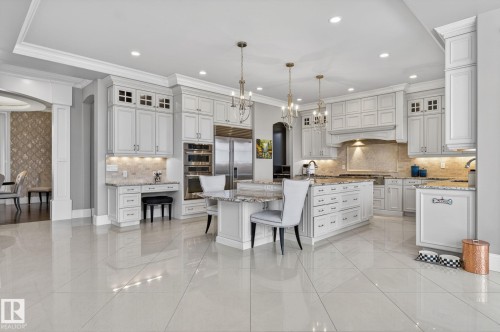 This spacious kitchen features light-colored cabinetry, a large central island with seating, stainless steel appliances, and polished tile flooring - 1413 Woodward Crescent, Edmonton, AB - Indoor Photo Showing Kitchen With Upgraded Kitchen