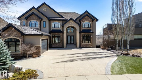 Stately stucco and stone exterior featuring a prominent arched entryway, multiple arched windows, a multi-car driveway with patterned concrete, a two-car garage, and a peaked roofline - 1413 Woodward Crescent, Edmonton, AB - Outdoor With Facade