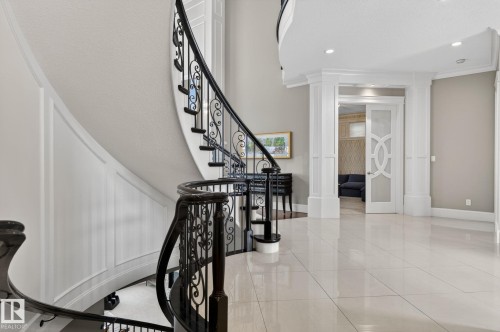 This property features a grand curved staircase with ornate black wrought iron balusters and a dark wood handrail, complemented by extensive white wainscoting - 1413 Woodward Crescent, Edmonton, AB - Indoor Photo Showing Other Room