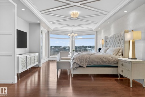 This spacious room features rich hardwood flooring, a unique coffered ceiling with a chandelier, and expansive windows offering a scenic view - 1413 Woodward Crescent, Edmonton, AB - Indoor Photo Showing Bedroom