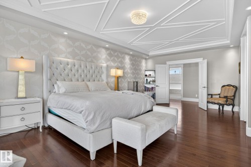 This bedroom features hardwood floors, a patterned accent wall, and a tray ceiling with decorative molding - 1413 Woodward Crescent, Edmonton, AB - Indoor Photo Showing Bedroom