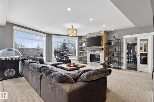 Spacious living area featuring large windows, a stone-faced fireplace with a television mounted above, and recessed lighting - 1413 Woodward Crescent, Edmonton, AB - Indoor Photo Showing Living Room With Fireplace