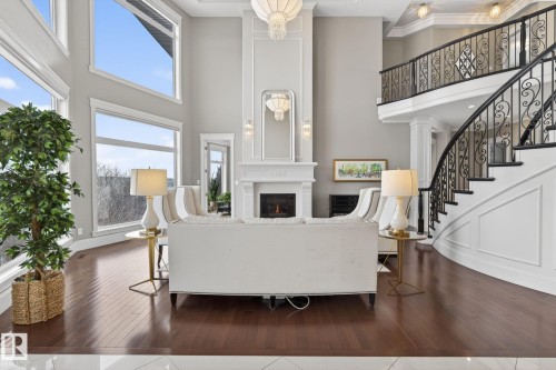 This living space features dark hardwood floors, a white fireplace with an ornate mantel and mirror, and tall windows that provide abundant natural light - 1413 Woodward Crescent, Edmonton, AB - Indoor Photo Showing Other Room With Fireplace