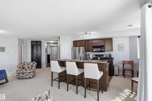 Open concept living area featuring light-colored carpet, a kitchen island with seating, and dark wood kitchen cabinetry - 115 6925 199 Street, Edmonton, AB - Indoor Photo Showing Kitchen