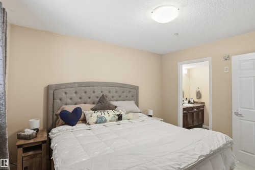 Well-appointed room featuring a ceiling light fixture, neutral colored walls, a padded headboard, and a wooden nightstand - 115 6925 199 Street, Edmonton, AB - Indoor Photo Showing Bedroom