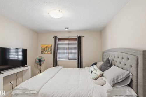 This room features a window with blinds and curtains, a light-colored headboard with button tufting, and a light-colored ceiling - 115 6925 199 Street, Edmonton, AB - Indoor Photo Showing Bedroom