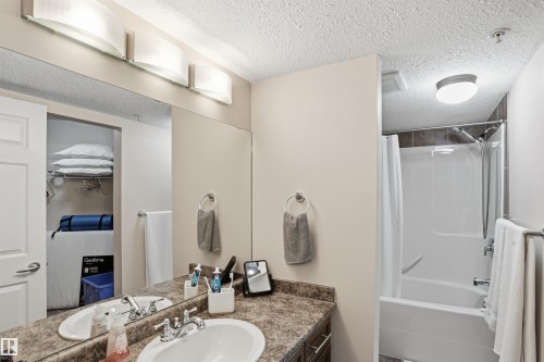 The bathroom features a vanity with a countertop and a white sink, illuminated by a three-light fixture - 115 6925 199 Street, Edmonton, AB - Indoor Photo Showing Bathroom