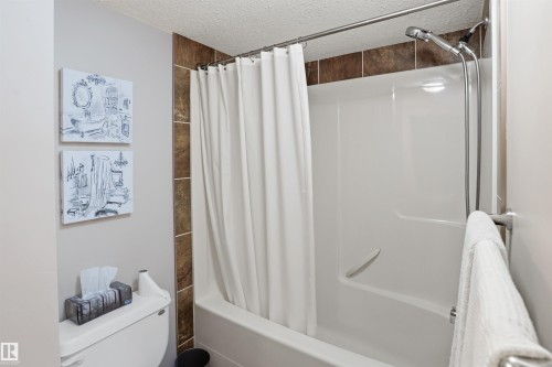 The bathroom features a bathtub with a shower, a shower curtain, and decorative wall tiles - 115 6925 199 Street, Edmonton, AB - Indoor Photo Showing Bathroom