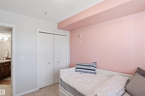 This room features neutral carpeting, a white bi-fold closet, and a light pink accent wall - 115 6925 199 Street, Edmonton, AB - Indoor Photo Showing Bedroom