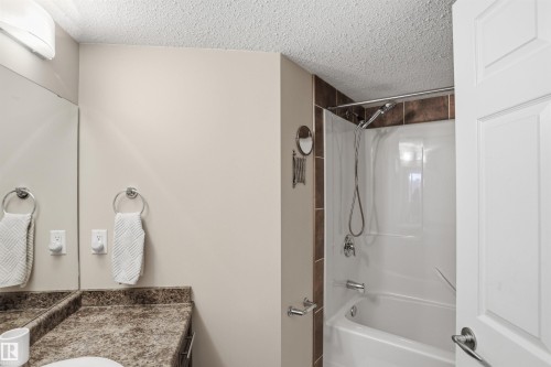 The bathroom features a vanity with a countertop, a mirror, and a shower/tub combination with tiled surround - 115 6925 199 Street, Edmonton, AB - Indoor Photo Showing Bathroom