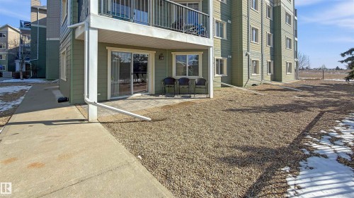The property features a ground-level patio with sliding glass doors, surrounded by a gravel area - 115 6925 199 Street, Edmonton, AB - Outdoor