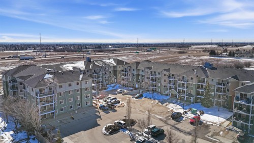 This property features a multi-story building with numerous balconies, a paved parking area, and a surrounding landscape with visible patches of snow - 115 6925 199 Street, Edmonton, AB - Outdoor With View