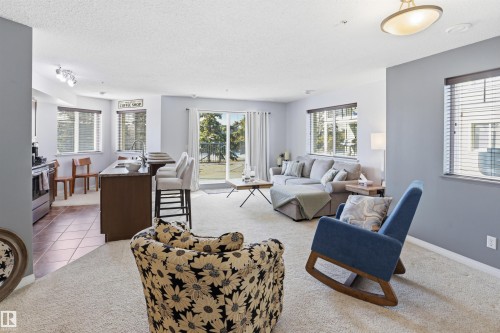 Open concept living area with carpet flooring, light gray walls, and large windows with blinds - 115 6925 199 Street, Edmonton, AB - Indoor Photo Showing Living Room