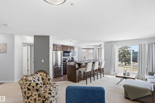 The property features an open-concept living area, including a kitchen with stainless steel appliances and dark wood cabinetry - 115 6925 199 Street, Edmonton, AB - Indoor