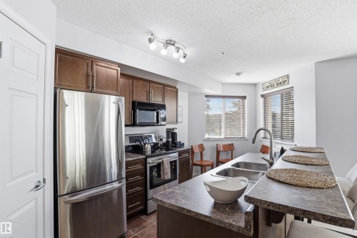 The kitchen features a stainless steel refrigerator, dark wood cabinetry, and a double basin sink - 115 6925 199 Street, Edmonton, AB - Indoor Photo Showing Kitchen With Double Sink With Upgraded Kitchen