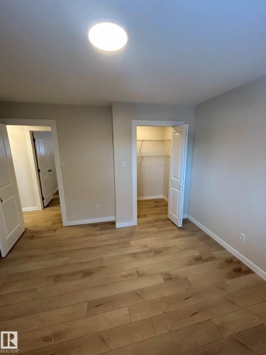 This space features light wood flooring, neutral tone walls, a ceiling-mounted light fixture, and an open closet with shelving - 56 Salisbury Avenue, St. Albert, AB - Indoor Photo Showing Other Room