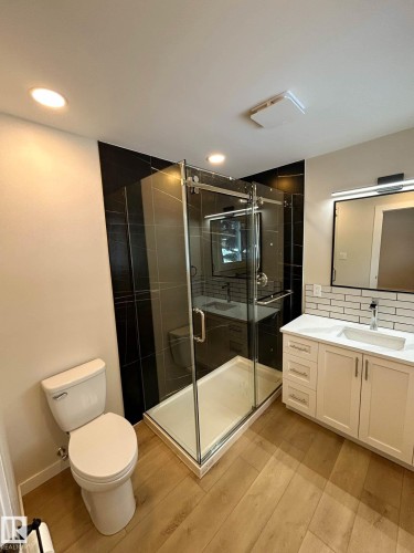 The bathroom features a glass-enclosed shower with dark tiled walls, a white vanity with a rectangular basin, and light-toned wood flooring - 56 Salisbury Avenue, St. Albert, AB - Indoor Photo Showing Bathroom