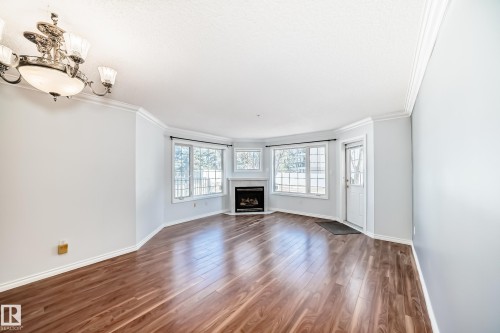 Living area featuring rich hardwood floors, a prominent fireplace with a light-colored mantel, and large windows providing natural light - 112 17150 94A Avenue, Edmonton, AB - Indoor Photo Showing Living Room With Fireplace
