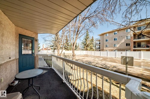 This property features a covered patio with a textured ceiling, a blue door with glass inserts, and a white railing - 112 17150 94A Avenue, Edmonton, AB - Outdoor With Exterior