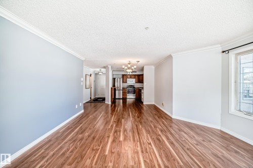 Open concept living area featuring hardwood flooring, crown molding, and a window providing natural light - 112 17150 94A Avenue, Edmonton, AB - Indoor Photo Showing Other Room