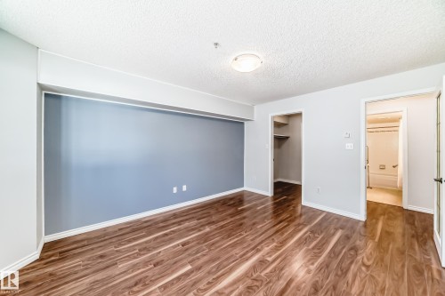 This room features rich wood flooring and a light blue accent wall - 112 17150 94A Avenue, Edmonton, AB - Indoor Photo Showing Other Room