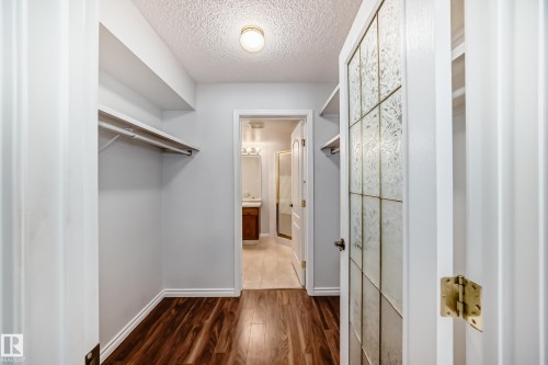 Walk-in closet featuring wood-look flooring, light-colored walls, and built-in shelving with hanging rods - 112 17150 94A Avenue, Edmonton, AB - Indoor Photo Showing Other Room