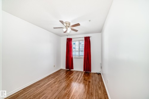 The room features hardwood floors, a window with red curtains, and a ceiling fan with integrated lighting - 112 17150 94A Avenue, Edmonton, AB - Indoor Photo Showing Other Room