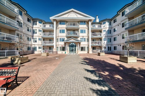 The property features multiple balconies, a brick paver courtyard, and a central entrance with an arched window - 112 17150 94A Avenue, Edmonton, AB - Outdoor With Facade