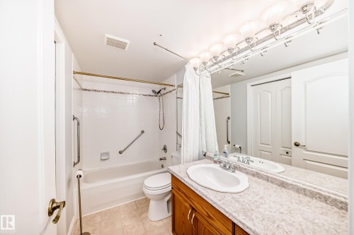 The bathroom features a vanity with a light-colored countertop and a built-in sink, a full-width mirror with overhead lighting, and a bathtub with white tiled walls - 112 17150 94A Avenue, Edmonton, AB - Indoor Photo Showing Bathroom