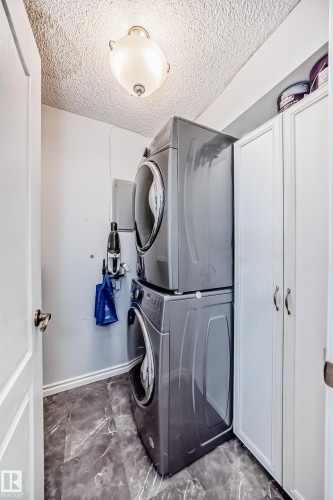 Dedicated laundry area featuring a stacked washer and dryer, white cabinetry, and patterned flooring - 112 17150 94A Avenue, Edmonton, AB - Indoor Photo Showing Laundry Room