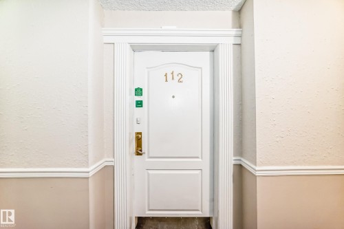 The property entrance features a white paneled door with a brass door handle and decorative trim - 112 17150 94A Avenue, Edmonton, AB - Indoor Photo Showing Other Room
