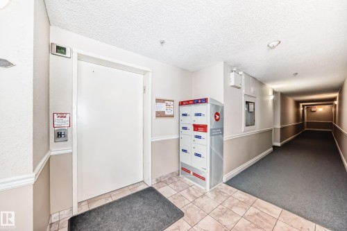 Building interior featuring a hallway with carpet flooring and wall molding, a tiled floor area, and a mail station - 112 17150 94A Avenue, Edmonton, AB - Indoor Photo Showing Other Room