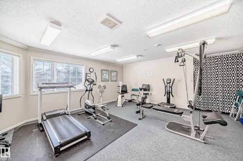 Well-equipped fitness area featuring various exercise machines, windows with blinds, and overhead lighting - 112 17150 94A Avenue, Edmonton, AB - Indoor Photo Showing Gym Room