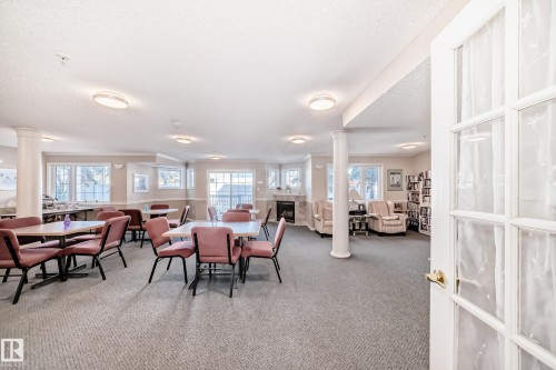 Spacious common area featuring carpet flooring, several tables with chairs, and a seating area with a fireplace - 112 17150 94A Avenue, Edmonton, AB - Indoor