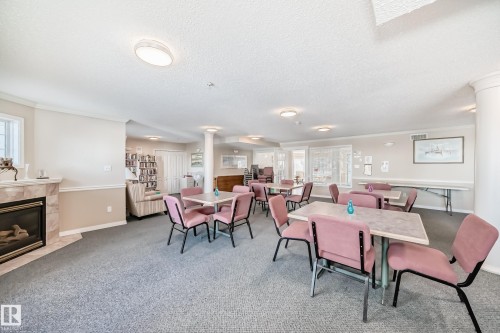 This room features a cozy fireplace with a stone surround, neutral wall tones with decorative wainscoting, and a carpeted floor - 112 17150 94A Avenue, Edmonton, AB - Indoor With Fireplace