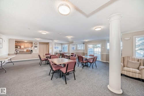 Spacious common area featuring carpet flooring, a kitchenette with wood cabinetry, and multiple windows providing natural light - 112 17150 94A Avenue, Edmonton, AB - Indoor