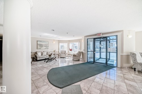 Inviting lobby area featuring tile flooring, a seating area with a sofa and armchairs, and automatic glass doors - 112 17150 94A Avenue, Edmonton, AB - Indoor Photo Showing Other Room